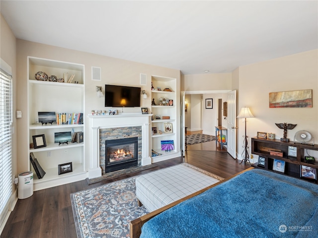 living room featuring a stone fireplace, built in shelves, and dark hardwood / wood-style flooring