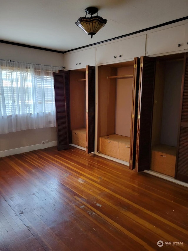 unfurnished bedroom featuring wood-type flooring and multiple closets