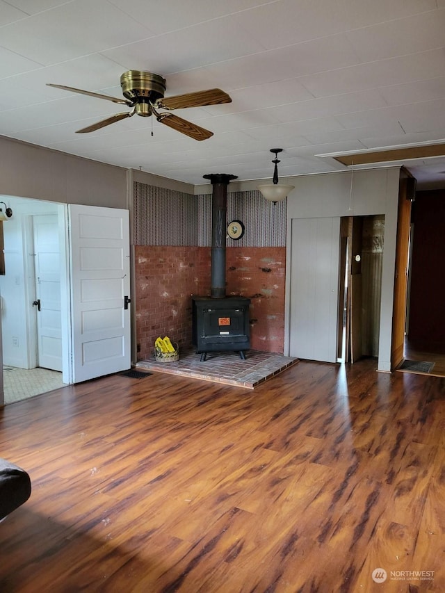 unfurnished living room with ceiling fan, hardwood / wood-style floors, and a wood stove