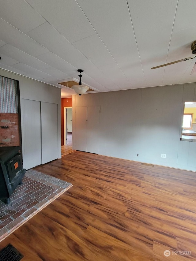 unfurnished living room with wood-type flooring, ceiling fan, and a wood stove