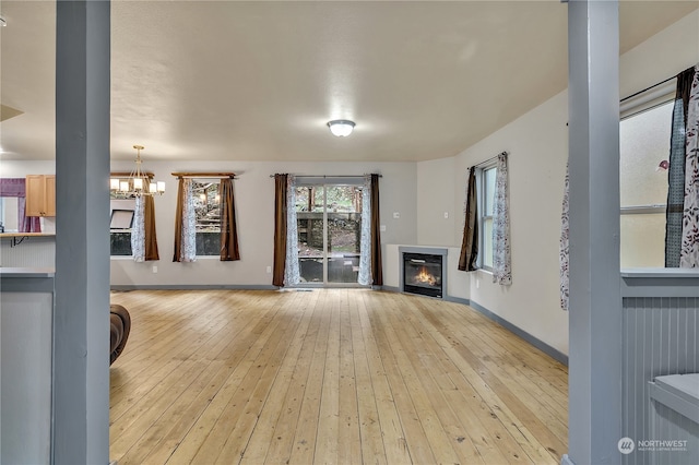 unfurnished living room featuring an inviting chandelier and light hardwood / wood-style flooring