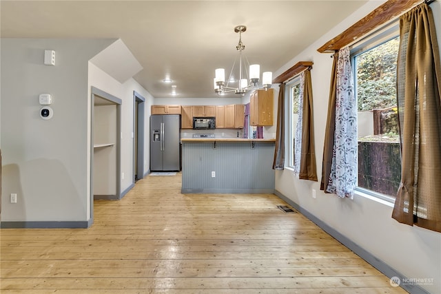 kitchen with plenty of natural light, stainless steel fridge with ice dispenser, kitchen peninsula, and decorative light fixtures