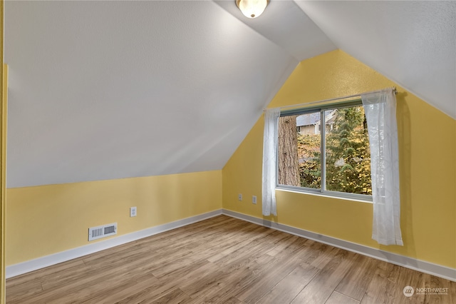 additional living space with vaulted ceiling, a textured ceiling, and light hardwood / wood-style flooring