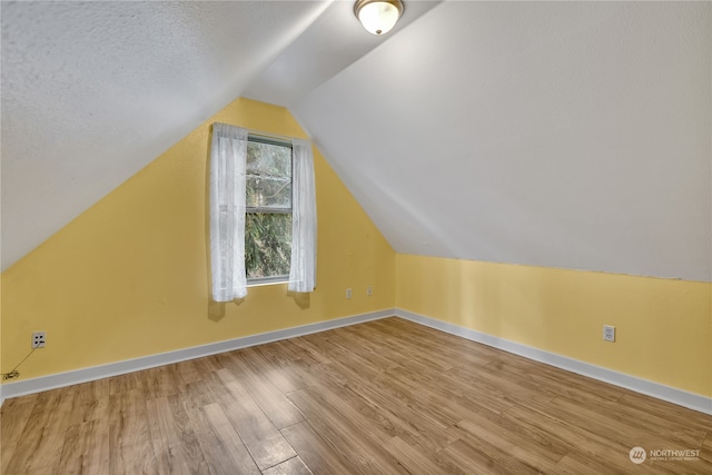 additional living space featuring hardwood / wood-style floors, a textured ceiling, and vaulted ceiling