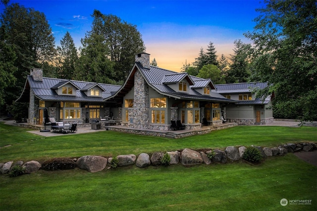 back house at dusk featuring a lawn and a patio area