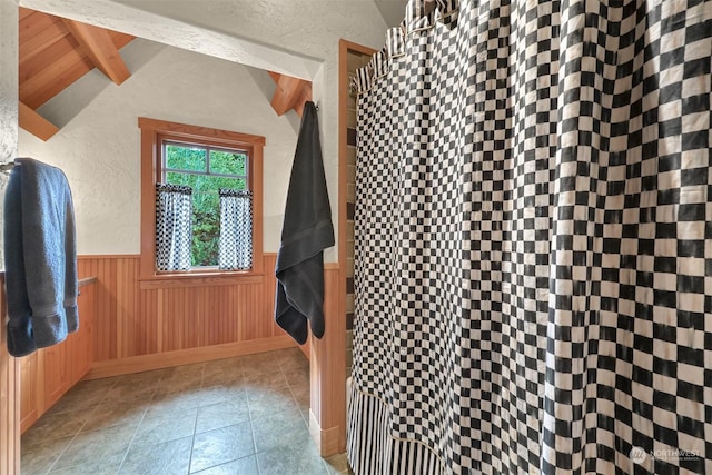 interior space with vaulted ceiling with beams, tile patterned floors, and wood walls