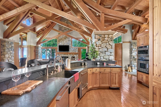 kitchen featuring sink, light hardwood / wood-style flooring, stainless steel appliances, a fireplace, and beamed ceiling