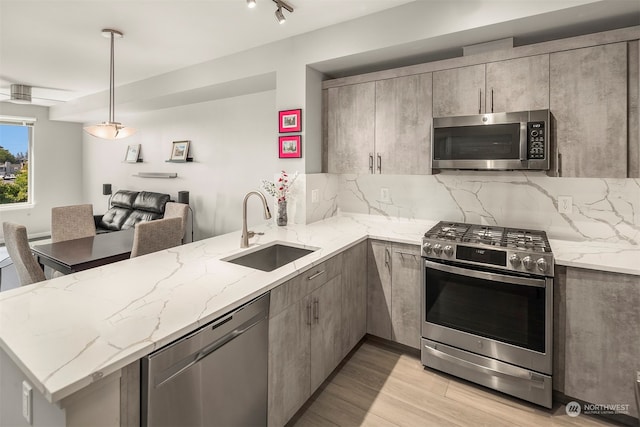 kitchen with stainless steel appliances, hanging light fixtures, decorative backsplash, sink, and light hardwood / wood-style floors