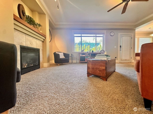 carpeted living room with ornamental molding, a tiled fireplace, and ceiling fan