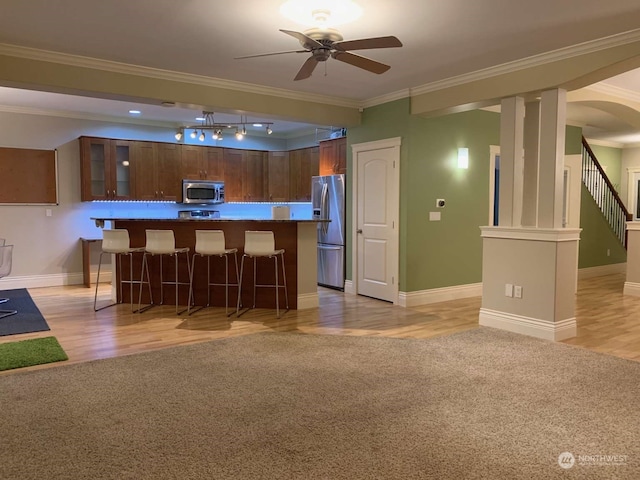 kitchen with light hardwood / wood-style floors, appliances with stainless steel finishes, a kitchen bar, and crown molding