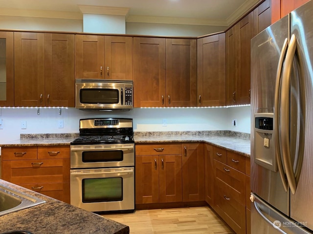 kitchen with appliances with stainless steel finishes, light wood-type flooring, stone counters, and ornamental molding