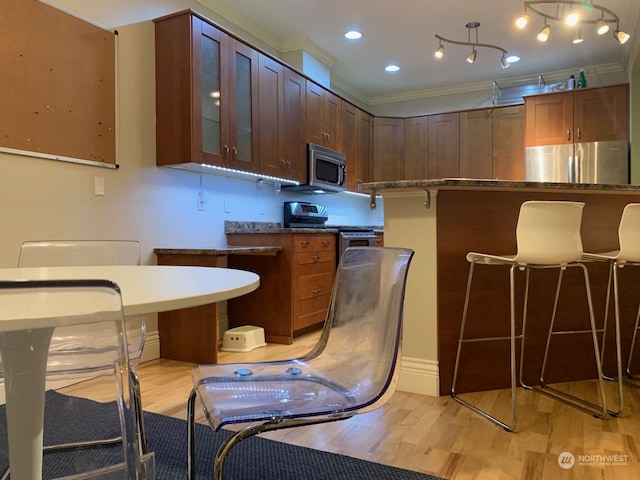 kitchen with dark stone counters, stainless steel appliances, light hardwood / wood-style floors, and crown molding