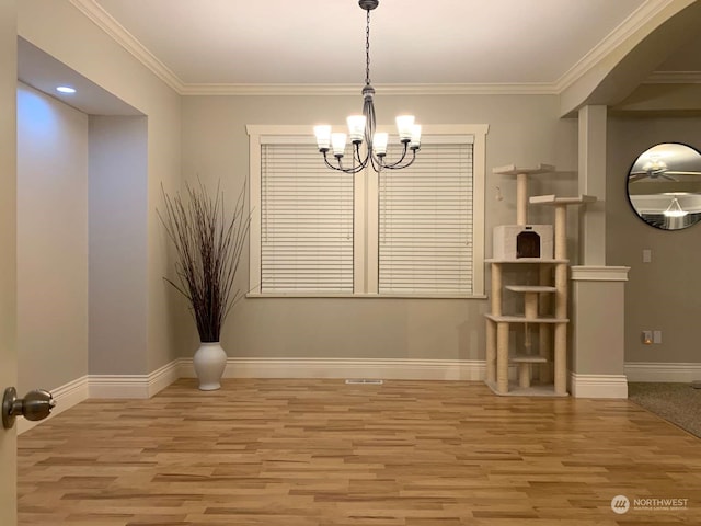 unfurnished dining area featuring wood-type flooring, crown molding, and an inviting chandelier