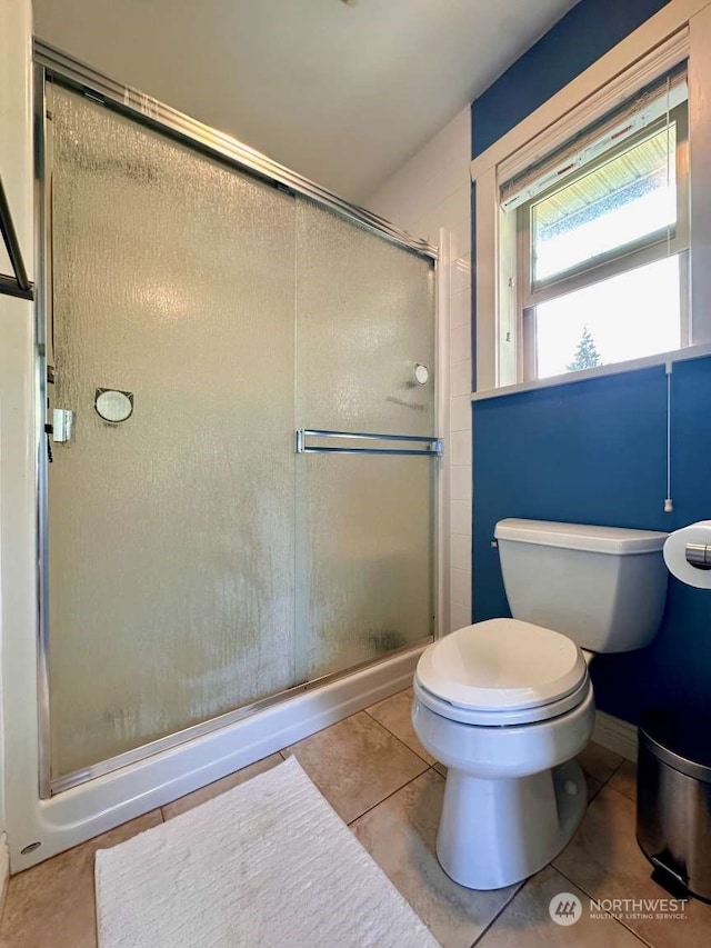 bathroom featuring a shower with door, tile patterned flooring, and toilet