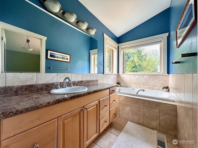 bathroom featuring a relaxing tiled tub, vanity, tile patterned flooring, and vaulted ceiling