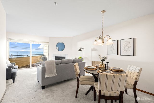 dining area featuring an inviting chandelier, a water view, light colored carpet, and a fireplace