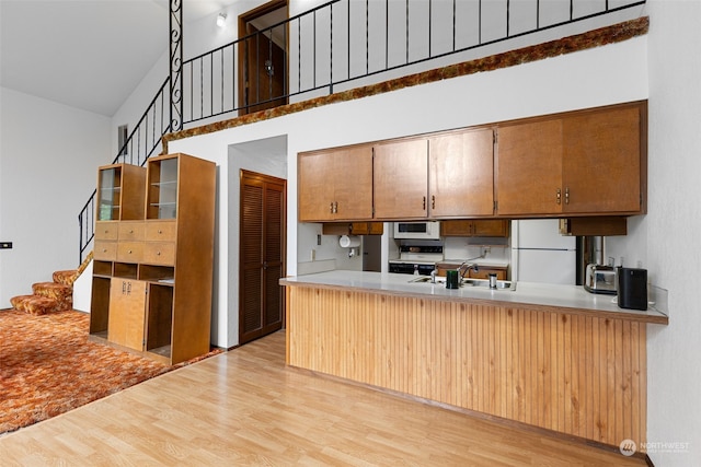 kitchen with sink, white appliances, kitchen peninsula, and light wood-type flooring