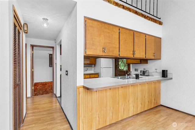 kitchen with sink, light wood-type flooring, kitchen peninsula, and white fridge