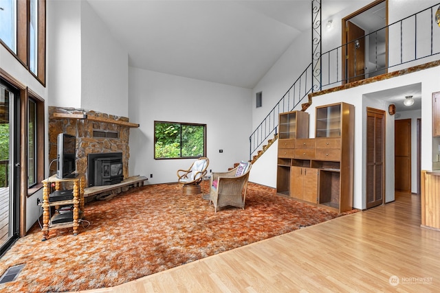 living room featuring high vaulted ceiling, a stone fireplace, and hardwood / wood-style floors