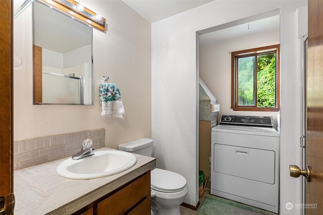 bathroom with vanity, toilet, washer / dryer, and a shower with shower door