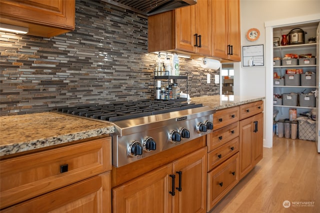 kitchen featuring backsplash, stainless steel gas cooktop, extractor fan, light hardwood / wood-style flooring, and light stone counters