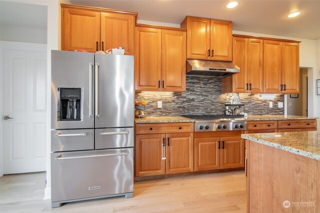 kitchen featuring decorative backsplash, light stone countertops, stainless steel appliances, and light hardwood / wood-style floors