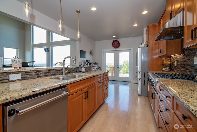 kitchen featuring light wood-type flooring, appliances with stainless steel finishes, sink, decorative backsplash, and wall chimney range hood