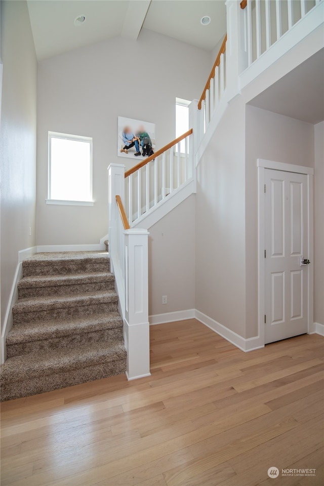 stairway with high vaulted ceiling and light wood-type flooring