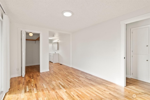 unfurnished bedroom featuring a spacious closet, a textured ceiling, a closet, and light wood-type flooring