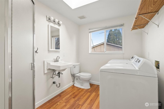 bathroom featuring hardwood / wood-style flooring, independent washer and dryer, toilet, and a skylight