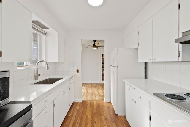 kitchen featuring sink, stovetop, white cabinetry, white refrigerator, and light wood-type flooring