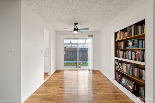 spare room with built in shelves, ceiling fan, light hardwood / wood-style flooring, and a textured ceiling