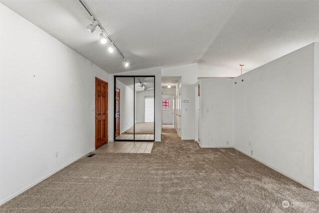 carpeted empty room featuring vaulted ceiling, track lighting, and a textured ceiling