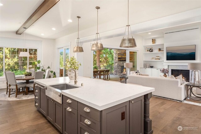 kitchen with pendant lighting, lofted ceiling with beams, sink, light stone countertops, and wood-type flooring