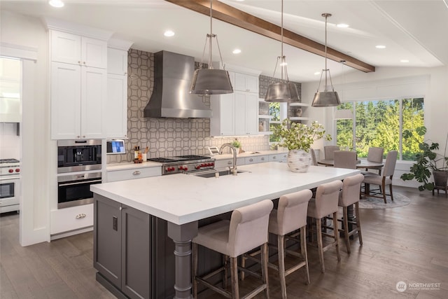 kitchen with white cabinetry, sink, wall chimney exhaust hood, tasteful backsplash, and an island with sink