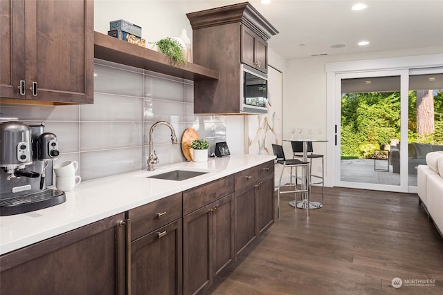 kitchen featuring dark hardwood / wood-style flooring, backsplash, dark brown cabinetry, sink, and stainless steel microwave