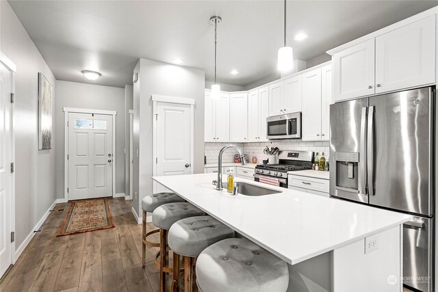 kitchen with tasteful backsplash, stainless steel appliances, a center island with sink, sink, and wood-type flooring