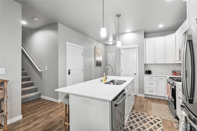 kitchen with stainless steel appliances, a center island with sink, sink, backsplash, and hardwood / wood-style flooring