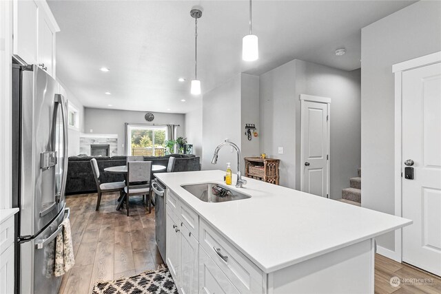 kitchen featuring appliances with stainless steel finishes, sink, light wood-type flooring, an island with sink, and white cabinetry