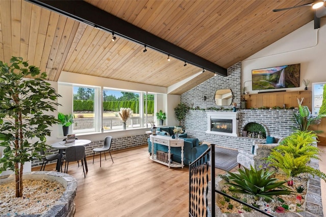 living area with lofted ceiling with beams, a brick fireplace, brick wall, wood finished floors, and wooden ceiling