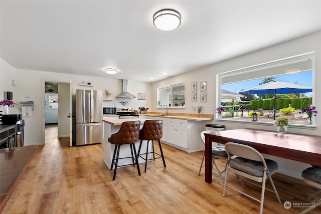 kitchen featuring a breakfast bar, light countertops, appliances with stainless steel finishes, a sink, and wall chimney exhaust hood