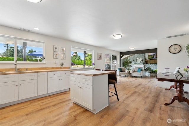 kitchen featuring light wood finished floors, butcher block countertops, a glass covered fireplace, and white cabinets