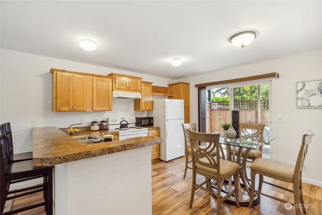 kitchen with white appliances, light wood-style flooring, a peninsula, under cabinet range hood, and a sink