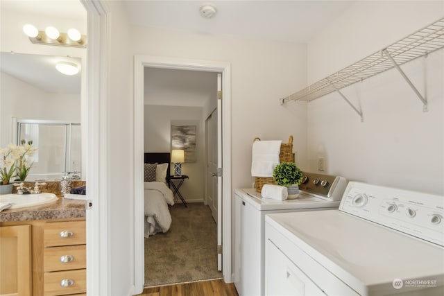 clothes washing area featuring washer and dryer, a sink, baseboards, and wood finished floors