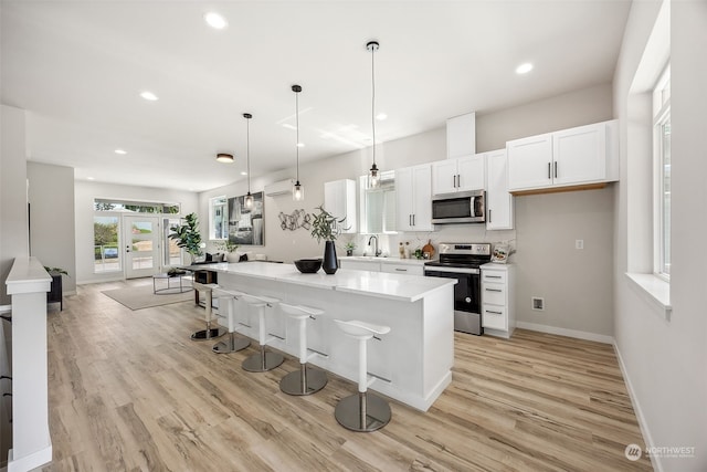 kitchen with appliances with stainless steel finishes, a kitchen breakfast bar, pendant lighting, a center island, and white cabinetry