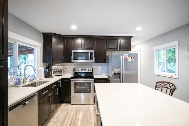 kitchen featuring appliances with stainless steel finishes, light countertops, a sink, and light wood-style flooring