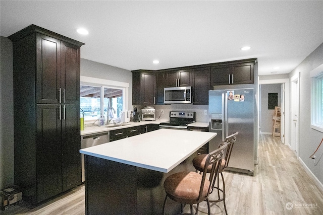 kitchen with a kitchen island, stainless steel appliances, dark brown cabinets, light countertops, and a sink