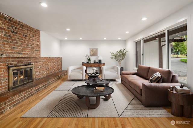 living room featuring light wood-type flooring, a fireplace, and brick wall