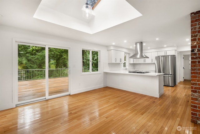 kitchen with light wood-type flooring, stainless steel fridge, white cabinetry, island range hood, and kitchen peninsula