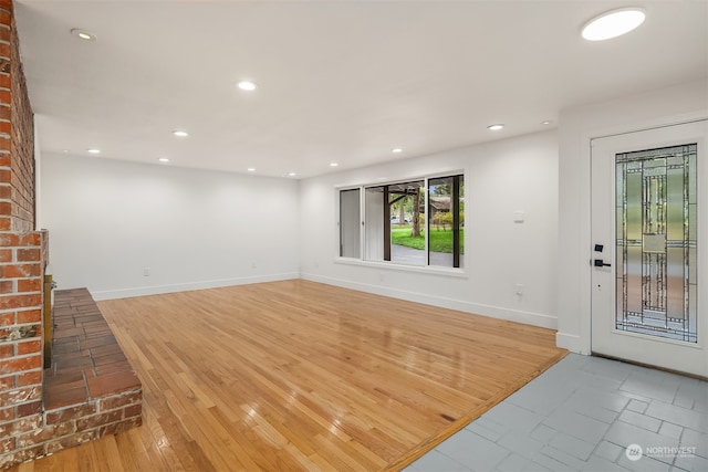 unfurnished living room with brick wall and light hardwood / wood-style flooring